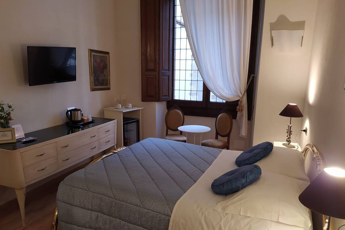 Een hotelkamer met een bed, een bureau, een televisie, een kleintje tafeltje, twee stoelen en een raam met gordijnen.