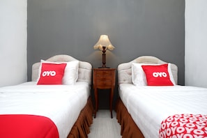 A hotel room with two beds, each with a red pillow labeled "OYO," a wooden nightstand with a lamp, and a white bedspread. - OYO 2055 Perdana Kasih (Klaten)
