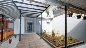 Un espacio al aire libre techado con suelo de baldosas, plantas en macetas y un banco de madera.
