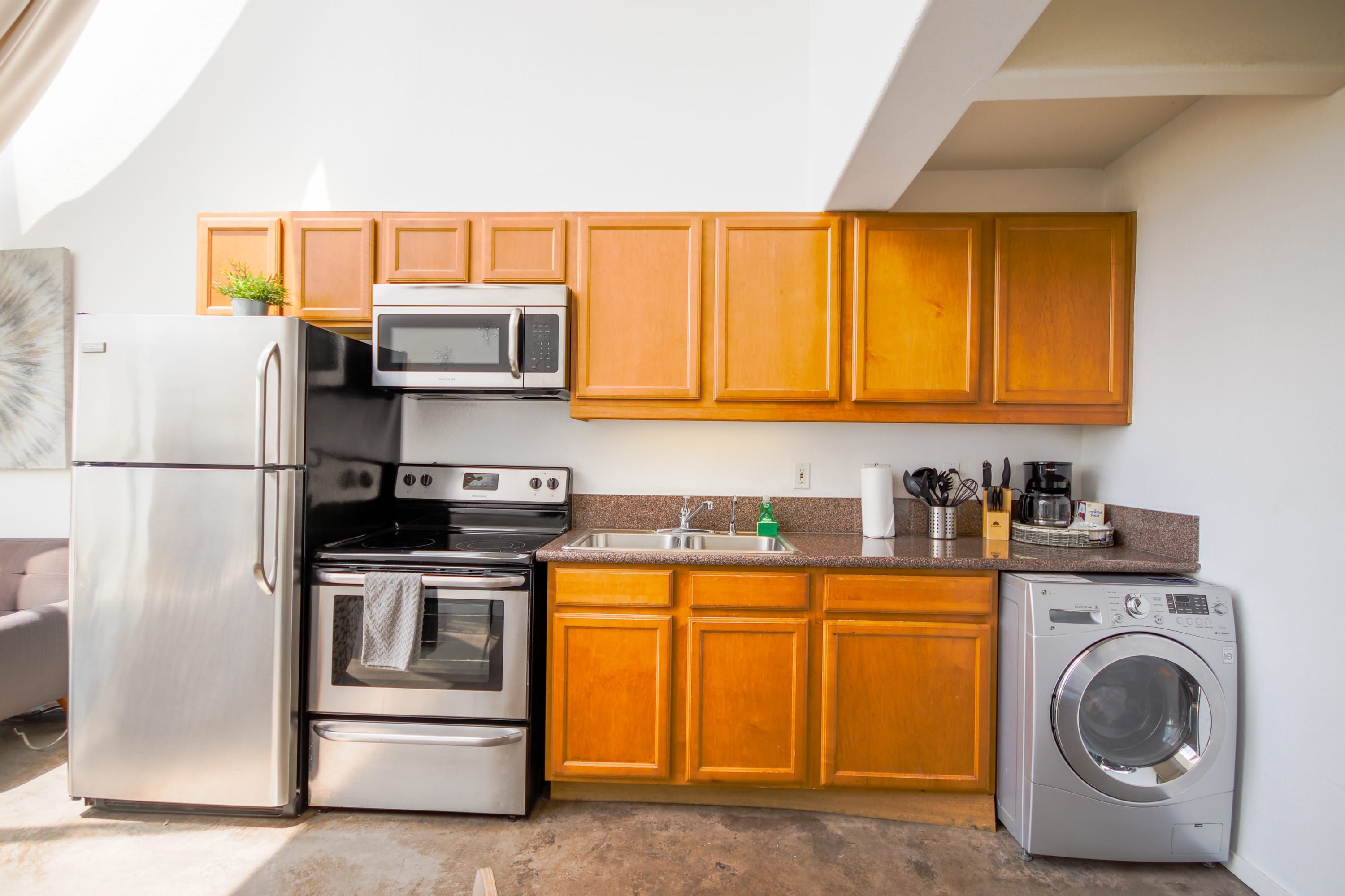 A compact kitchen with stainless steel appliances, wooden cabinets, and a built-in washer.