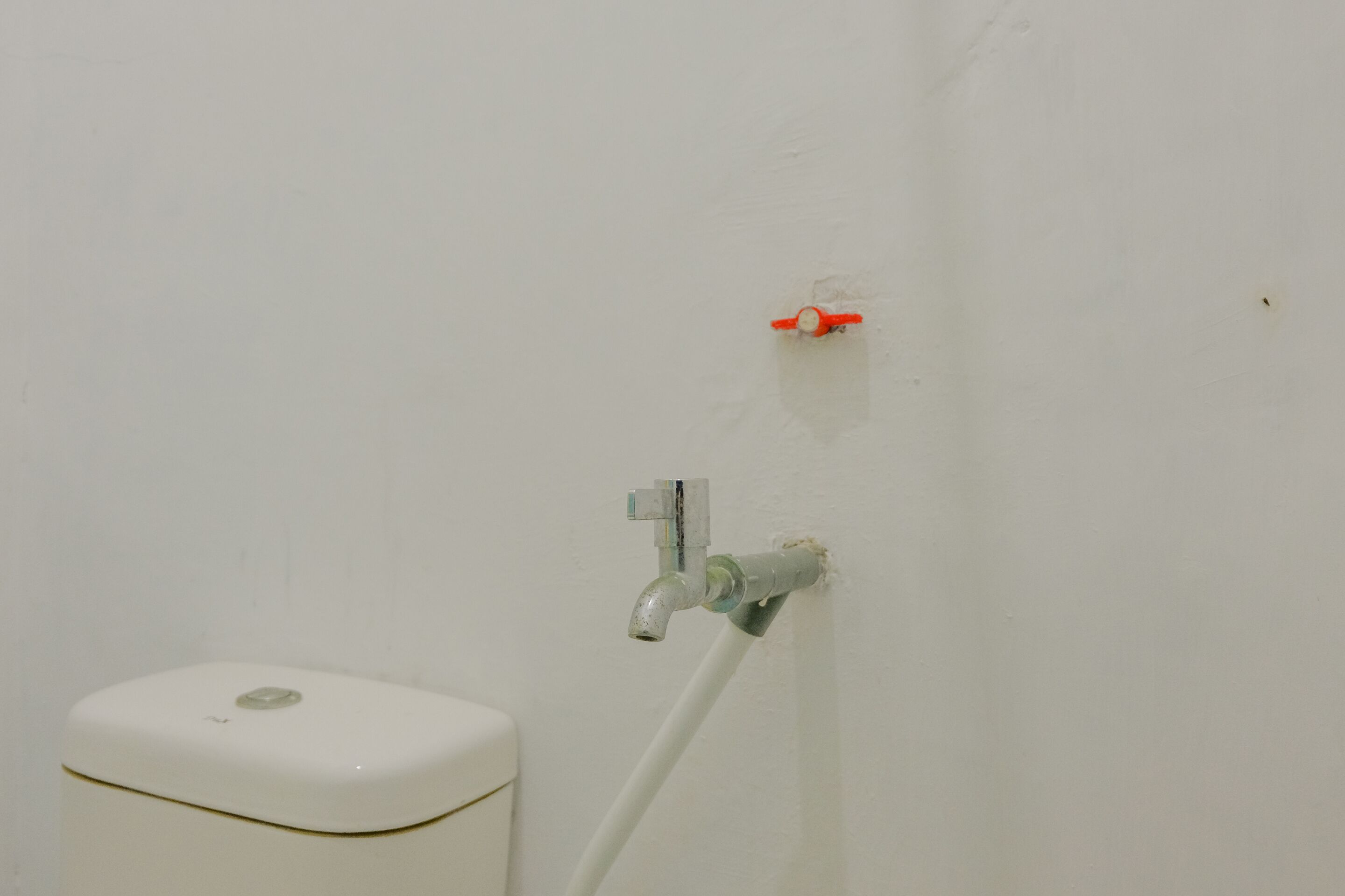 A white toilet with a flush handle and a visible pipe running along the wall.