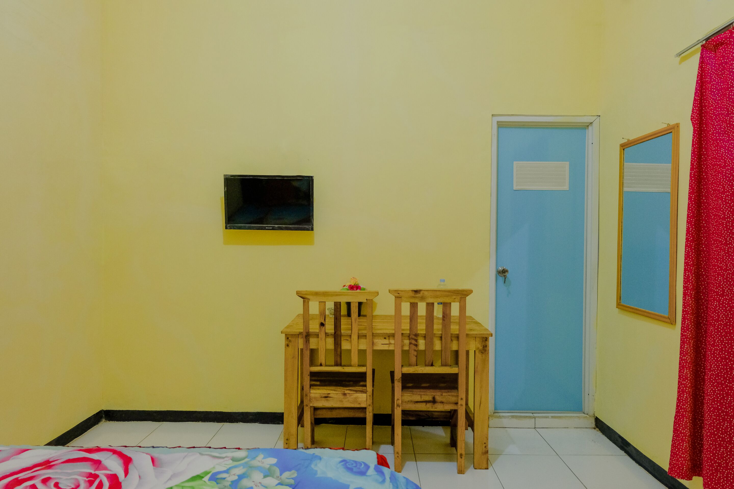 Una habitación con una cama, una pequeña mesa con dos sillas, una puerta azul y una cortina roja.