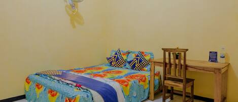 A bedroom with a bed, a wooden chair, a small table, and a wall-mounted fan.