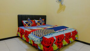 A bed with a colorful bedspread and pillows, a wall-mounted fan, and a tiled floor. - SPOT ON 1976 Hamana Beach Inn (Pacitan)