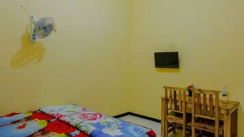 Una habitación con una cama, una mesita pequeña con una silla, un ventilador de pared y un televisor.