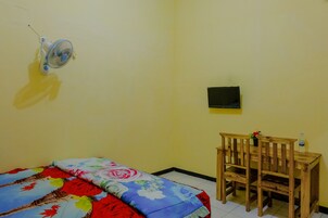 Una habitación con una cama, una mesita pequeña con una silla, un ventilador de pared y un televisor.