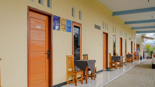 A corridor with wooden doors, a tiled floor, and a row of tables and chairs. - SPOT ON 1976 Hamana Beach Inn (Pacitan)
