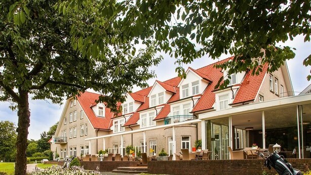 A row of traditional European-style houses with red-tiled roofs, a covered outdoor seating area, and a well-maintained garden. - Ahauser Land-&Golfhotel (Ahaus)