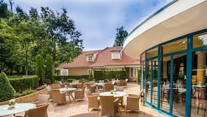 An outdoor patio area with wicker furniture and a glass enclosure. - Ahauser Land-&Golfhotel (Ahaus)