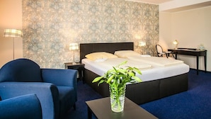 A hotel room with a bed, bedside lamps, a desk, a chair, and a vase with green plants. - Ahauser Land-&Golfhotel (Ahaus)
