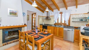 A kitchen with wooden cabinets, a dishwasher, and a dining area with a table set for two. - SON VADO rural finca for 4 people in Santa Margarita with pool (Santa Margalida)
