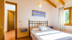 A bedroom with a bed, a nightstand, a wall-mounted light, and a wooden door. - SON VADO rural finca for 4 people in Santa Margarita with pool (Santa Margalida)