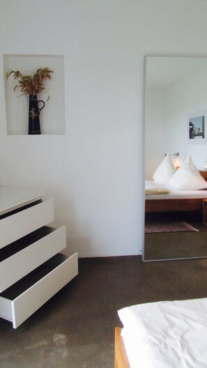 A modern bedroom with a bed, a mirror, and a white dresser with drawers. - Beltblick (Fehmarn)