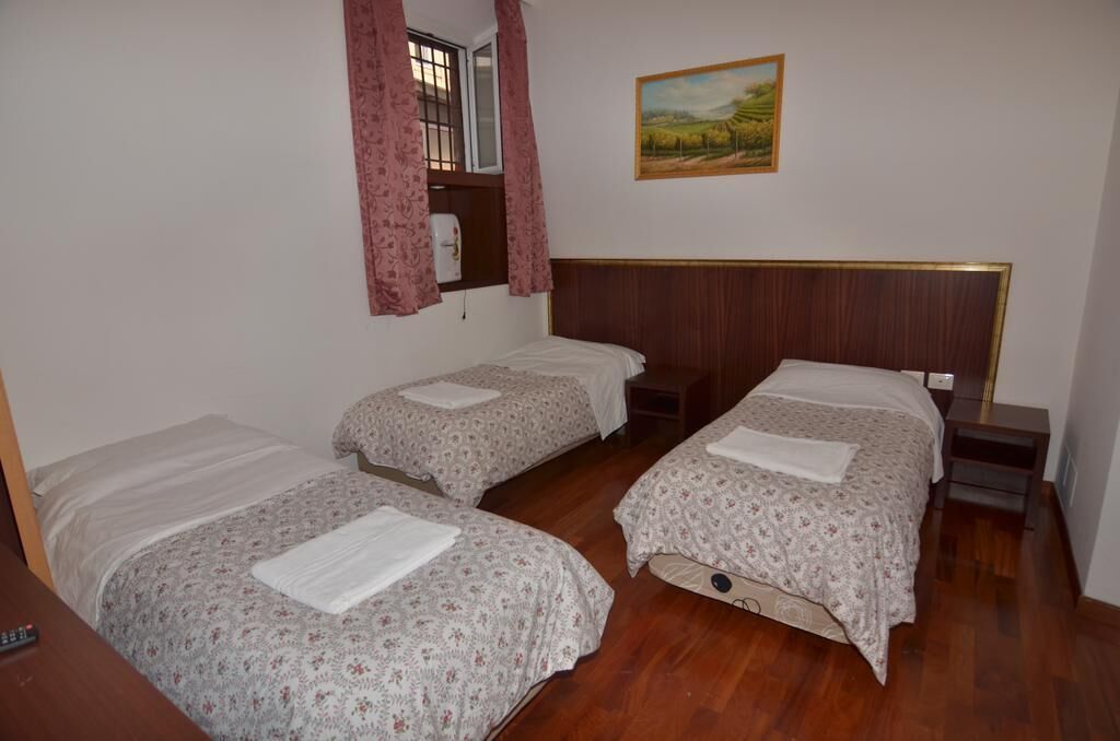 A room with two single beds, a wooden headboard, a painting on the wall, and a window with curtains.