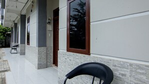 A clean, tiled hallway with a black chair in the foreground, a door with a brown frame, and a window reflecting trees. - OYO 2069 Wisma Syariah Kampung Baru (Rantauprapat)