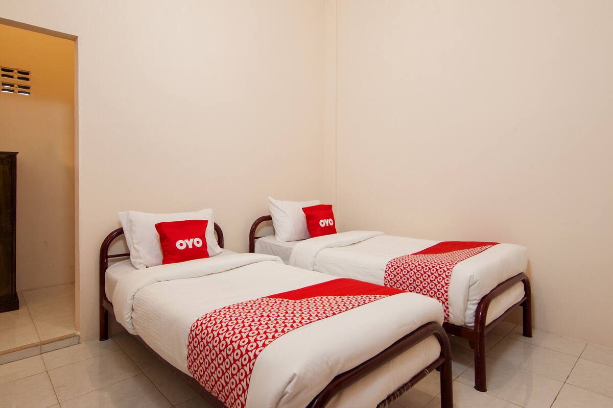 A hotel room with two single beds, each with a red and white patterned bedspread and matching pillows.