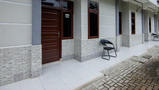 A building with a tiled entrance, a brown door, and a small outdoor seating area with a chair. - OYO 2069 Wisma Syariah Kampung Baru (Rantauprapat)