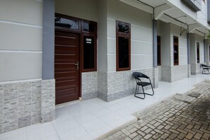 A building with a tiled entrance, a brown door, and a small outdoor seating area with a chair. - OYO 2069 Wisma Syariah Kampung Baru (Rantauprapat)