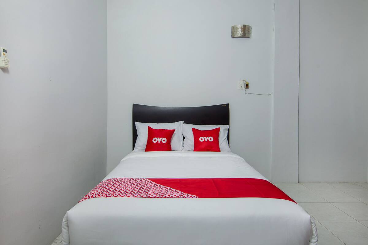 A bed with a white and red bedspread, two red pillows with the word "OYO" on them, and a black headboard.