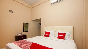 A hotel room with a bed, a nightstand, a mirror, and an air conditioning unit. - OYO 2069 Wisma Syariah Kampung Baru (Rantauprapat)
