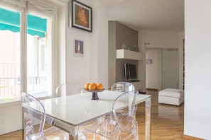 A modern living room with a white table, clear chairs, a fireplace, and a balcony with a green awning.