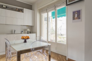 A modern kitchen with white cabinets, a glass dining table, and a view of the outside through a large window.