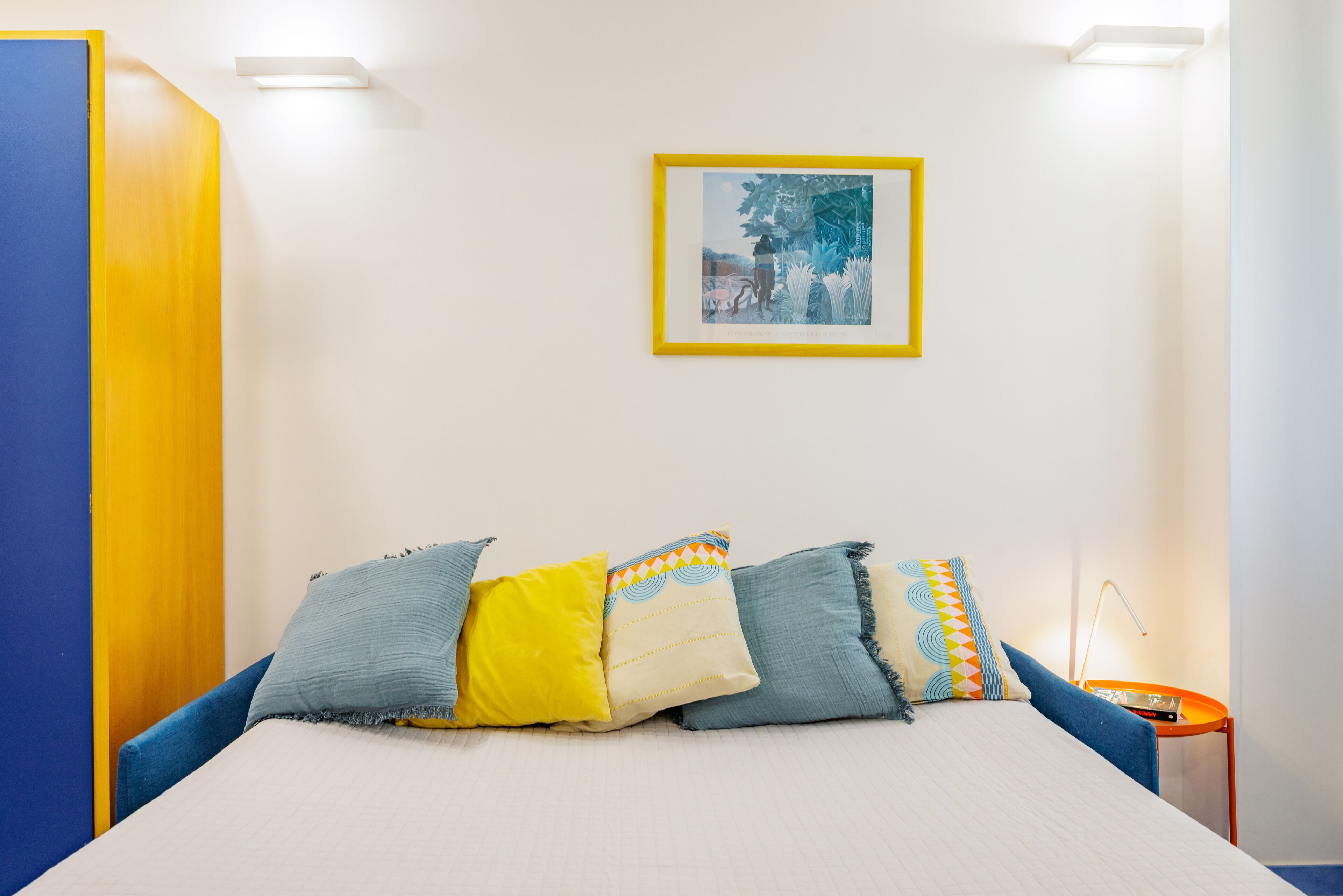 A bedroom with a bed, pillows, a nightstand, a lamp, and a framed picture on the wall.