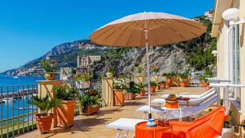 A terrace with a view of the sea, outdoor furniture, and potted plants.