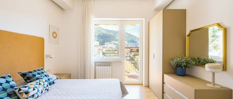 A bedroom with a bed, a dresser, a mirror, and a window with a view of buildings.