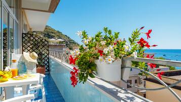 A balcony with a table set for breakfast, potted plants, and a view of the sea.
