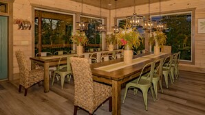 A wooden cabin interior with a large dining table, wicker chairs, and hanging chandeliers. - Ridge Top Retreat: Mtn Views, Indoor Pool, Theater, Games, Hot Tub, Wifi (Sevierville)