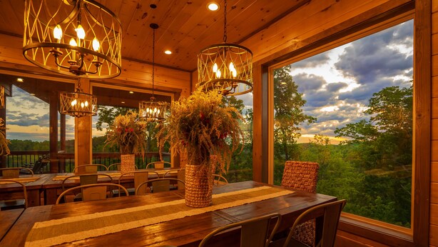 A wooden dining area with a large table, chairs, and hanging light fixtures. - Ridge Top Retreat: Mtn Views, Indoor Pool, Theater, Games, Hot Tub, Wifi (Sevierville)