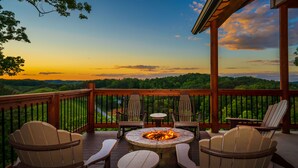 A deck with Adirondack chairs and a central fire pit, overlooking a scenic landscape. - Ridge Top Retreat: Mtn Views, Indoor Pool, Theater, Games, Hot Tub, Wifi (Sevierville)