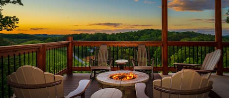 A deck with Adirondack chairs and a central fire pit, overlooking a scenic landscape.