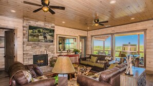 A spacious living room with leather sofas, a fireplace, and large windows offering a view of the outdoors. - Ridge Top Retreat: Mtn Views, Indoor Pool, Theater, Games, Hot Tub, Wifi (Sevierville)