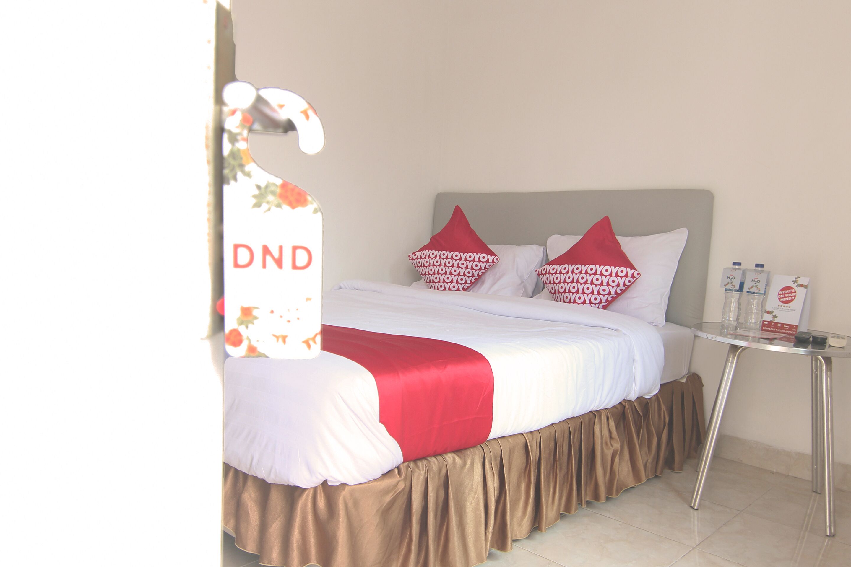A hotel room with a bed, pillows, a table with bottles, and a sign with the letters "DND".