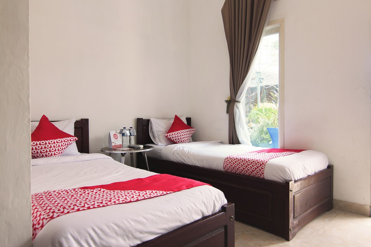 A hotel room with two beds, each with red and white patterned bedding, a small table with toiletries, and a window with curtains.