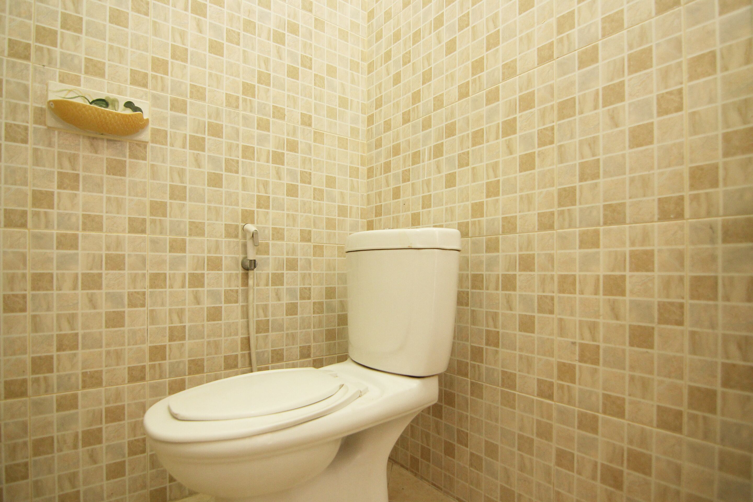 Ein Badezimmer mit Toilette, gefliesten Wänden und einer kleinen Ablage mit einer Obstschale.