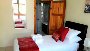 Een hotelkamer met een bed, een spiegel, een houten deur en een douche.