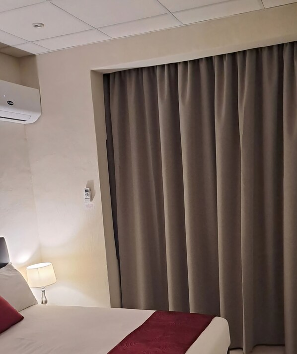 A hotel room with a bed, a lamp, a wall-mounted air conditioner, and a large window with curtains. - 85 PALMA LIVING- VICTORIA GOZO OLD TOWN CENTER (Ir-Rabat Għawdex)