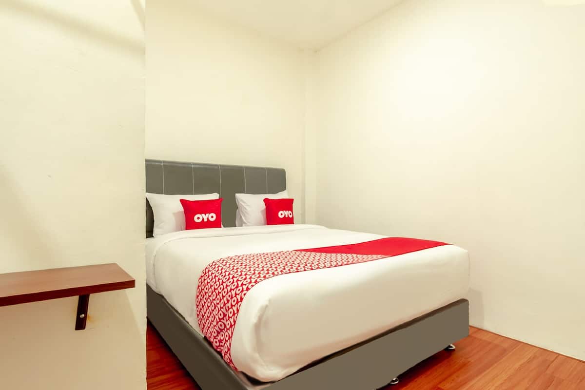 Een net opgemaakt bed met een deken in wit en rood, twee kussens met de tekst 'OYO' erop, en een grijs hoofdbord.