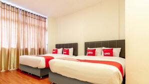 Une chambre d’hôtel avec deux lits, chacun doté d’un sommier gris et de draps blancs, d’oreillers rouges et d’une couverture à rayures rouges et blanches.