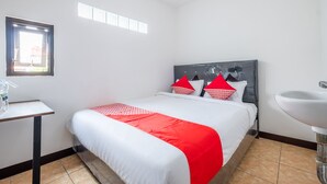 Een hotelkamer met een bed, nachtkastje, raam en een badkamerspiegel.