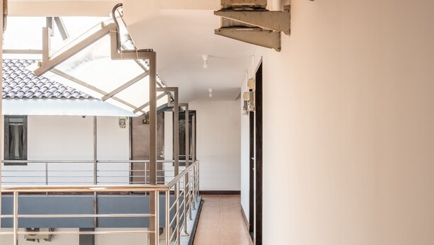 Een gang met een metalen hekwerk, een betegelde vloer en een uitzicht op een gebouw met een pannendak.