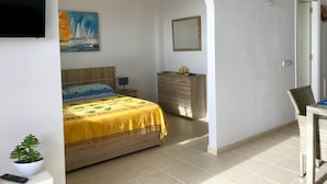 Quarto com cama, penteadeira, televisão, pintura e uma pequena planta.