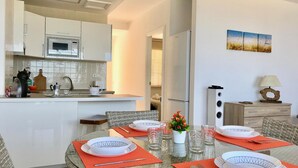 Uma cozinha moderna com armários brancos e uma área de jantar com mesa de vidro posta para quatro pessoas.