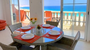 Espaço de refeições com mesa posta para quatro pessoas, com vista para a praia.