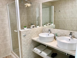 A modern bathroom with two sinks, a glass shower enclosure, and a large mirror.