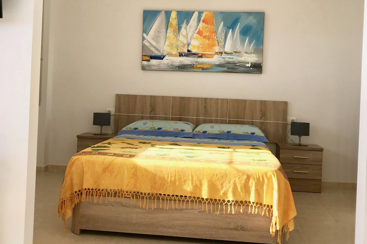 Quarto com cama, mesas de cabeceira, um quadro e cabeceira de madeira.