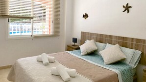 Quarto com uma cama, almofadas, mesa de cabeceira e estrelas-do-mar decorativas na parede.